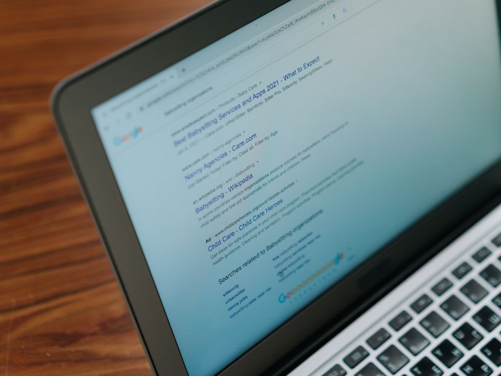 Tela de notebook exibindo resultados de busca no Google sobre serviços de babá, com destaque para links e anúncios relacionados a babysitting.