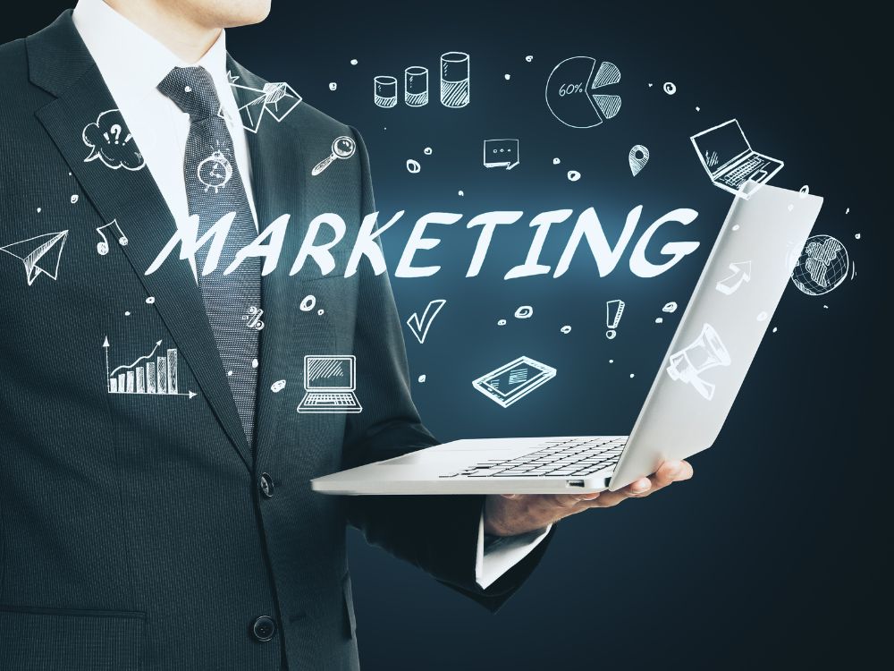 Texto alt: Profissional segurando notebook com elementos gráficos de marketing digital, gráficos, ícones e estratégias de comunicação ao fundo.