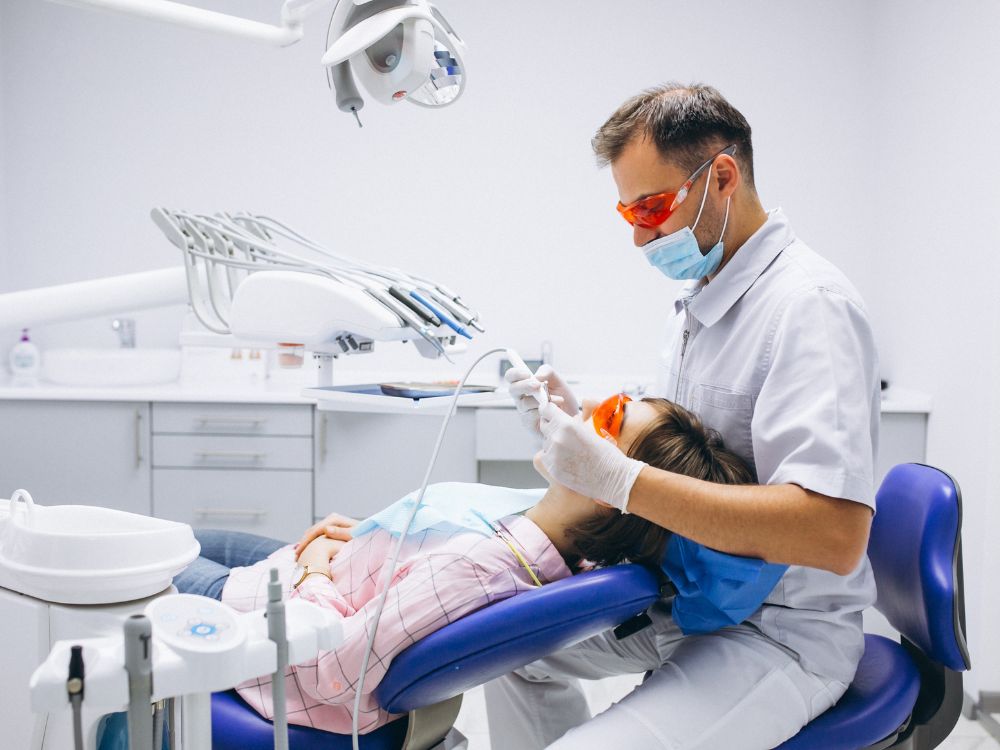 Dentista realizando atendimento clínico em consultório odontológico com equipamentos de proteção, imagem relacionada às exigências e procedimentos da norma dentista.